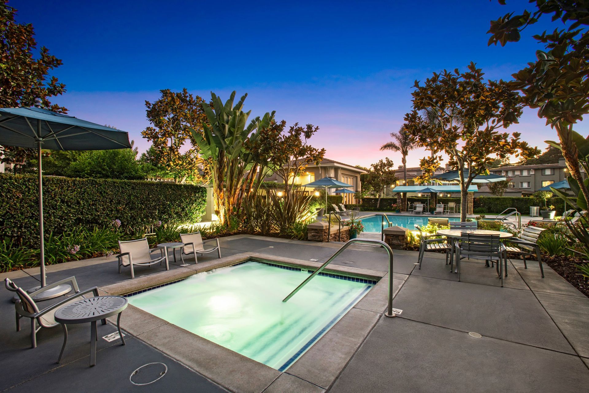 Outdoor community pool area with lounge chairs and umbrellas at dusk.