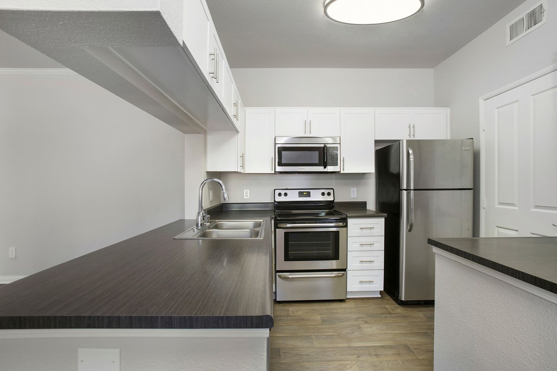 Modern kitchen in an apartment with white cabinets, stainless steel appliances, and dark countertops.