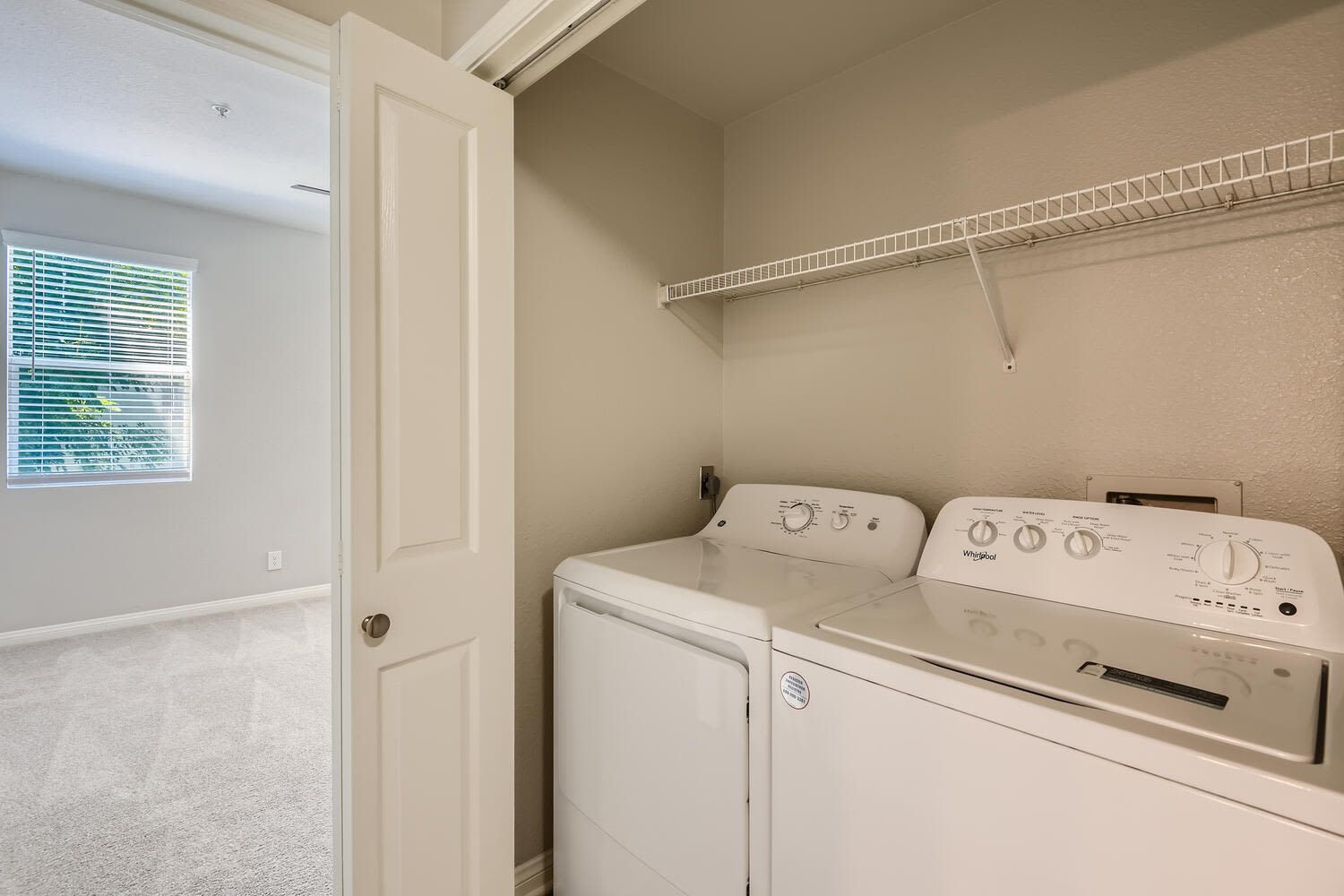 Laundry closet with washer and dryer and a wire shelf above.