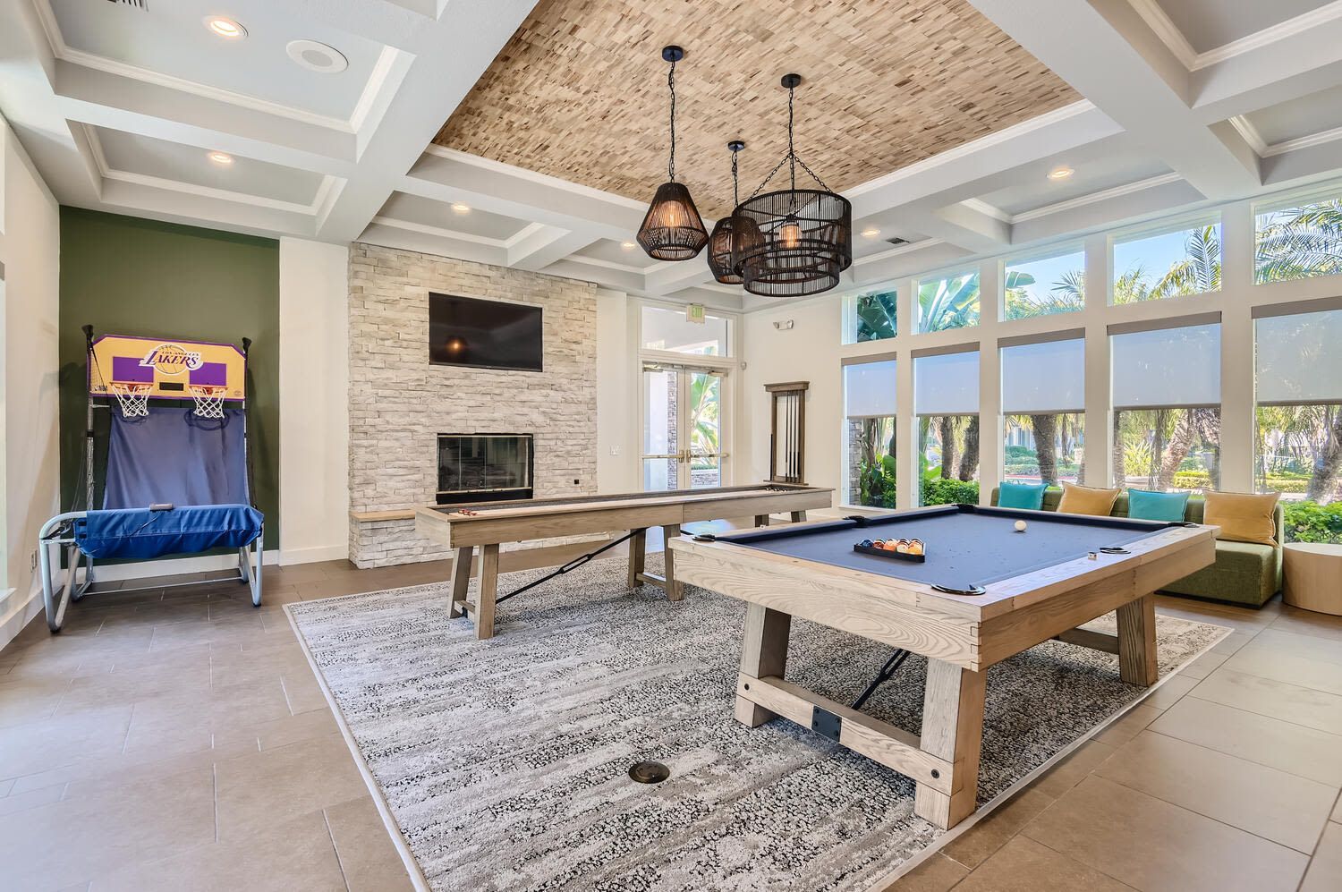 Indoor community game room with a pool table, long shuffleboard table, and seating by large windows.