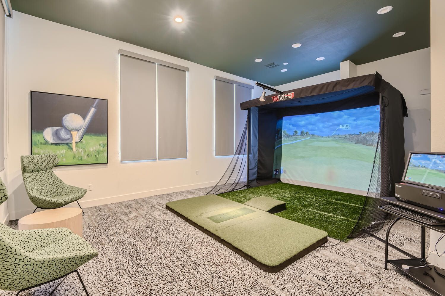 Indoor golf simulator in a recreation room with a large screen, turf mat, and seating.