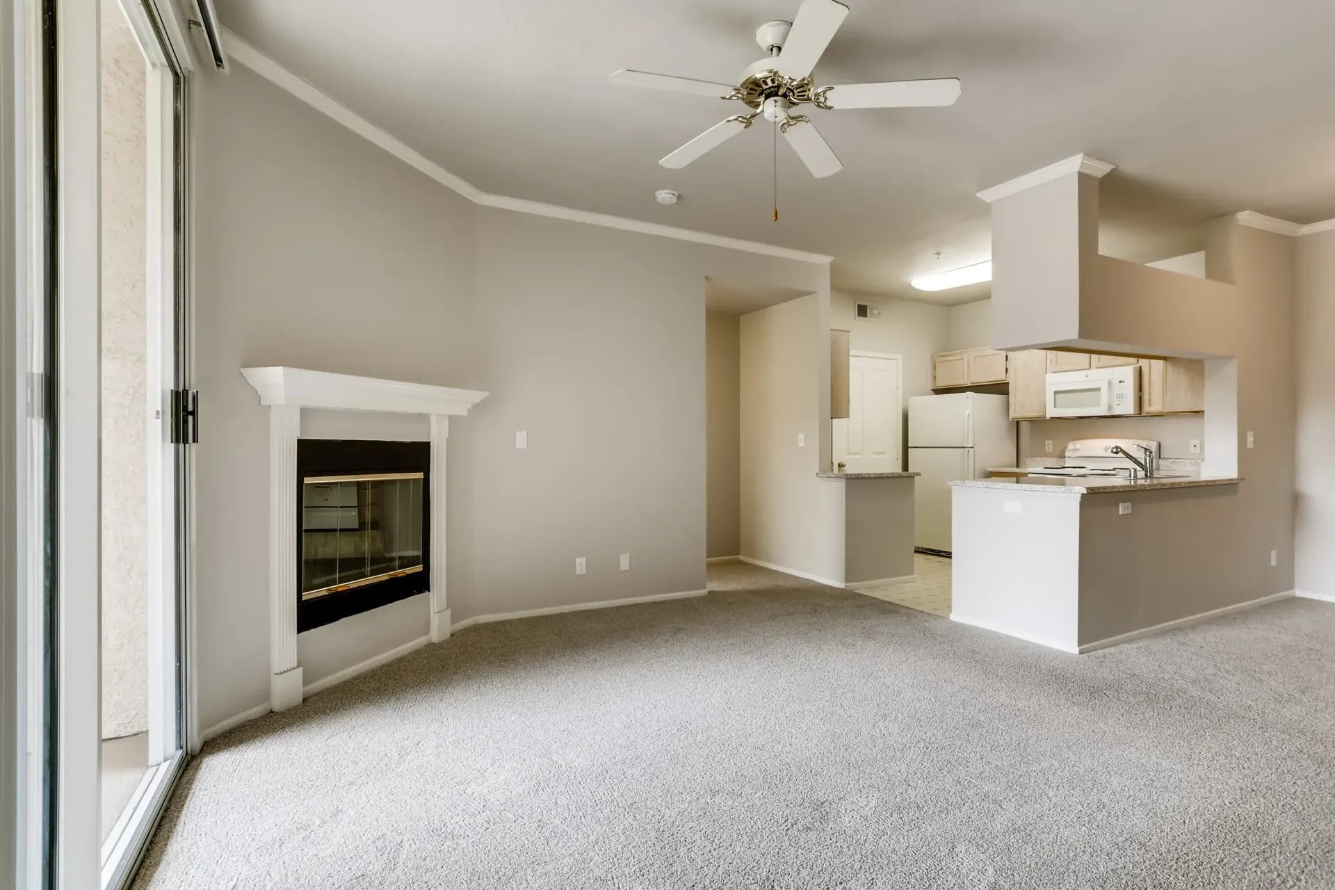 Living room with carpet, ceiling fan, and fireplace; open to the kitchen.