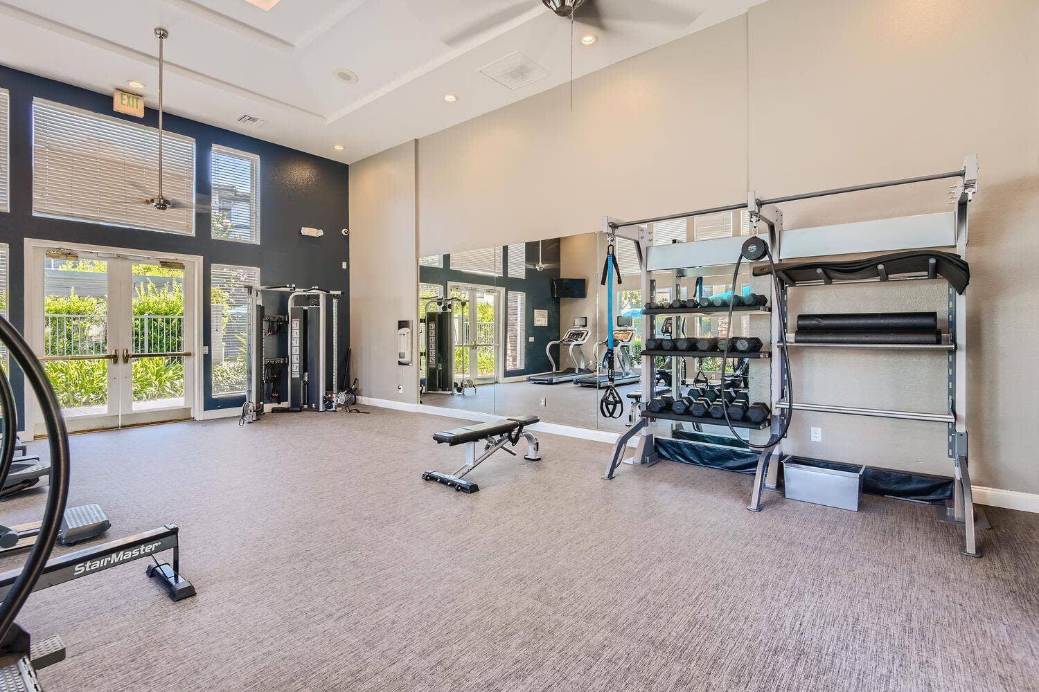 Well-lit community gym with free weights, a weight rack, treadmills, and a large mirror.