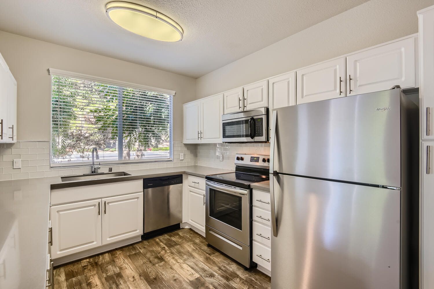 Modern apartment kitchen with white cabinets, stainless steel appliances, and a large window.