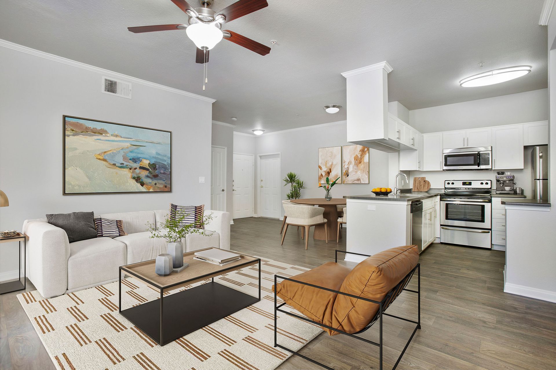 Open-concept living room and kitchen in a modern apartment with white cabinets and stainless appliances.