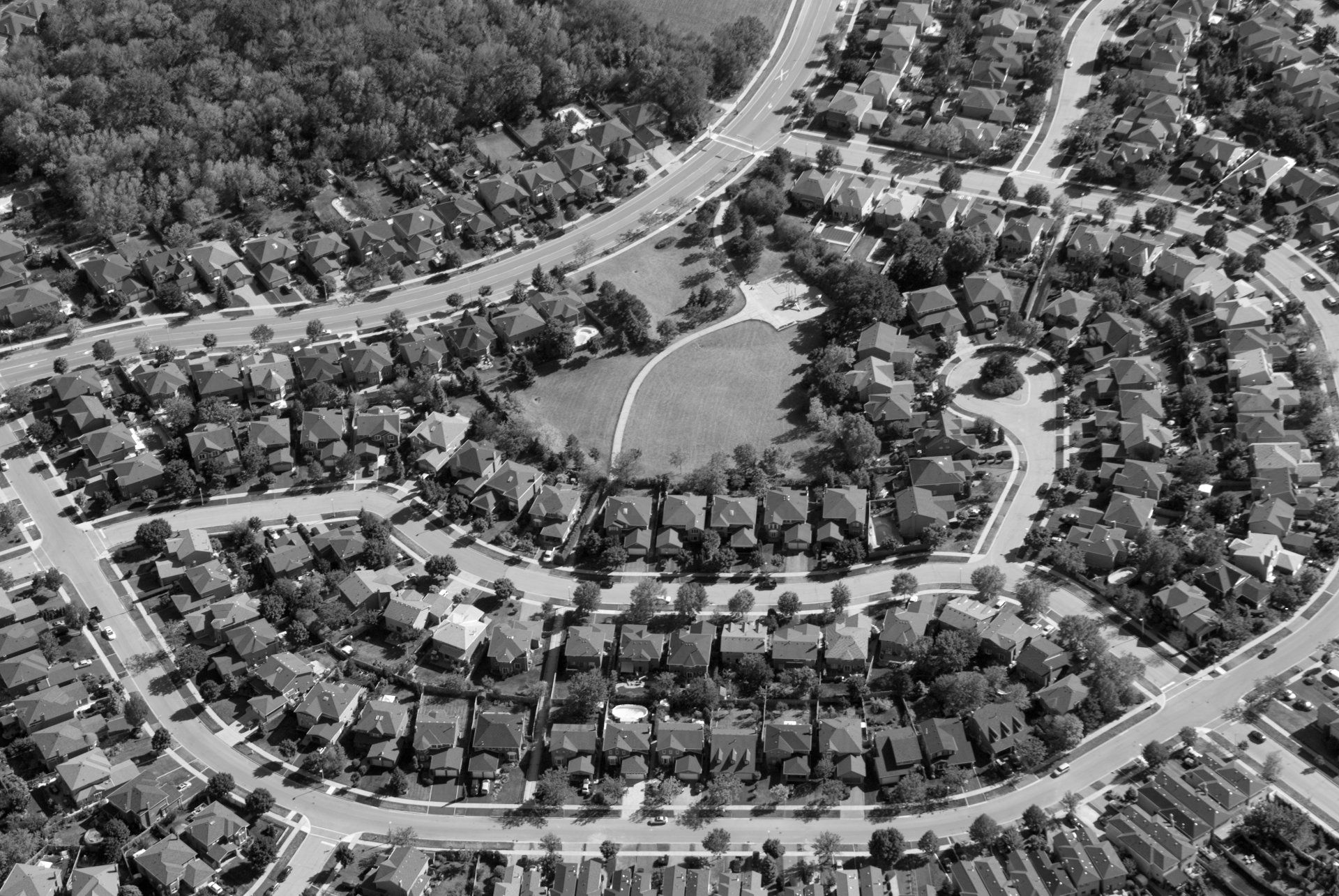 Vue aérienne d'un quartier résidentiel de banlieue avec des rues courbes, des maisons, des arbres et un petit parc.