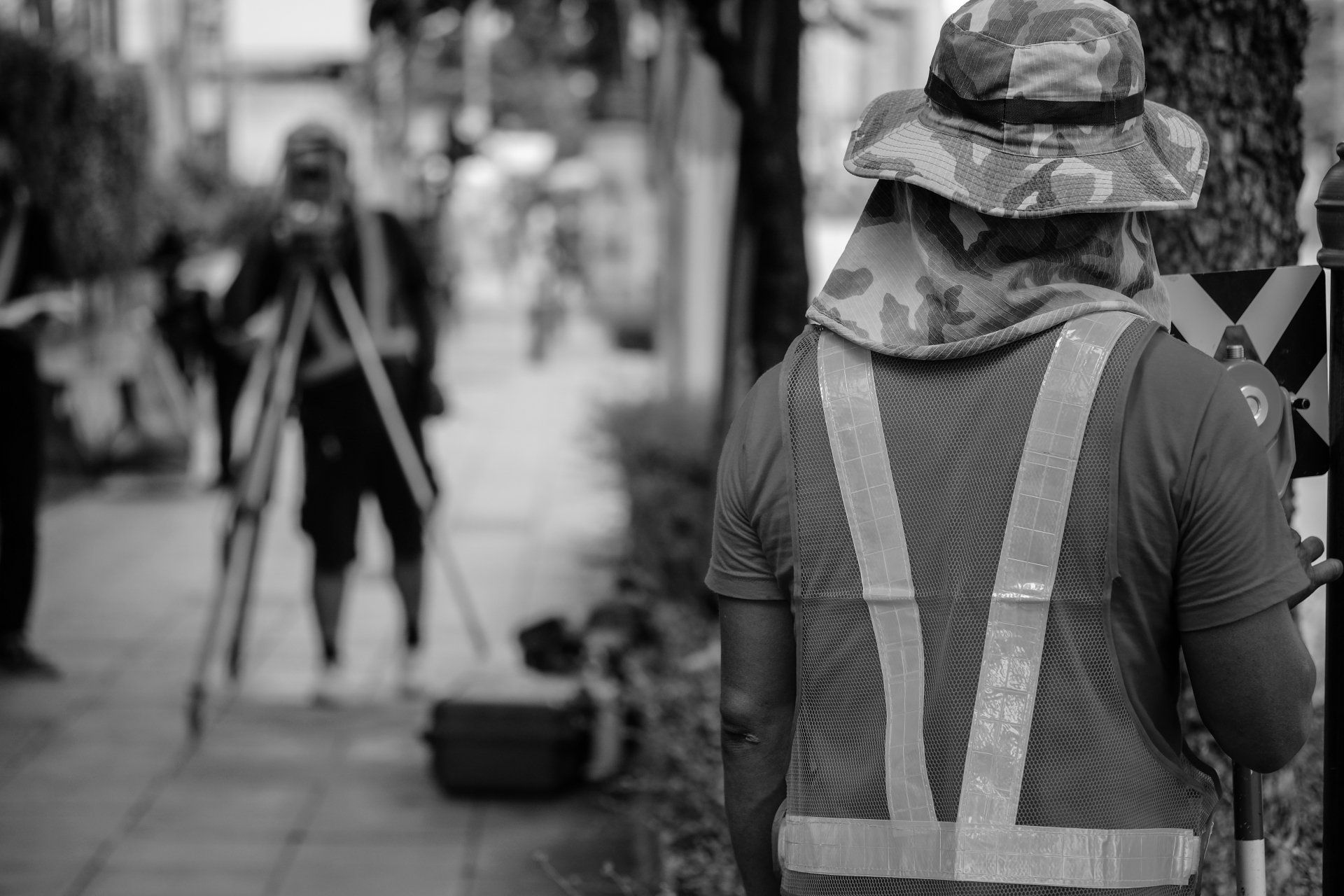 A black and white photo of a man wearing a safety vest and hat.
