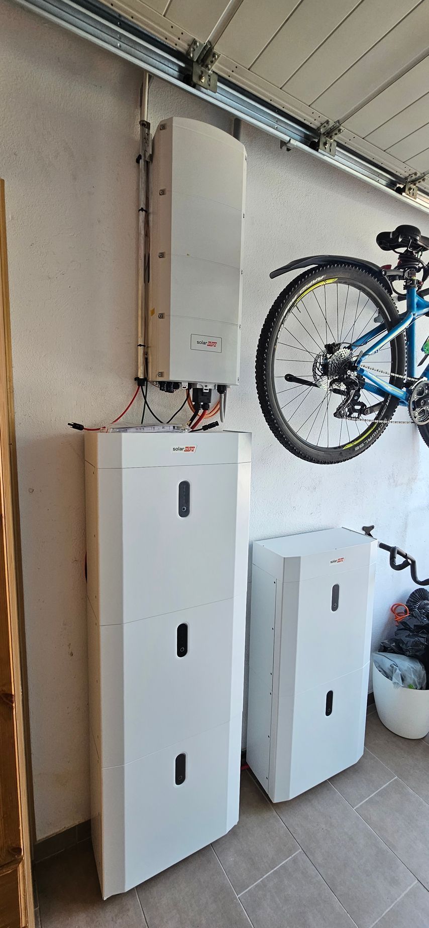 In einer Garage hängt neben einem Stromspeicher an der Wand ein Fahrrad.
