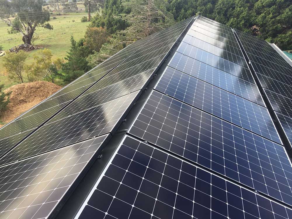 A Row Of Solar Panels On A Roof With Trees — Goulburn Solar In Goulburn, NSW