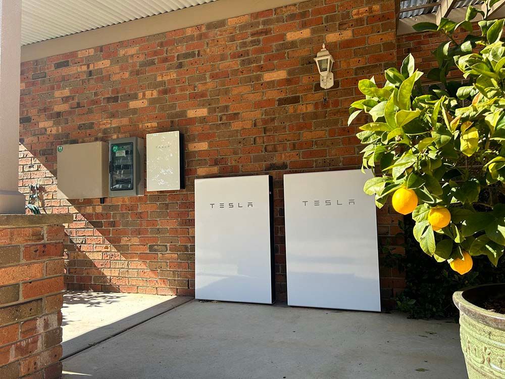 Two Tesla Batteries On The Side Of A Brick Building — Goulburn Solar In Goulburn, NSW