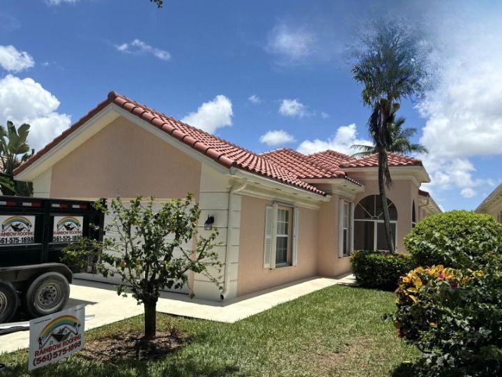 House with pink stucco, red tile roof, and palm tree being trimmed by a worker on a lift.