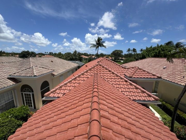 Red tile roofs of houses under a blue sky with puffy clouds and palm trees.