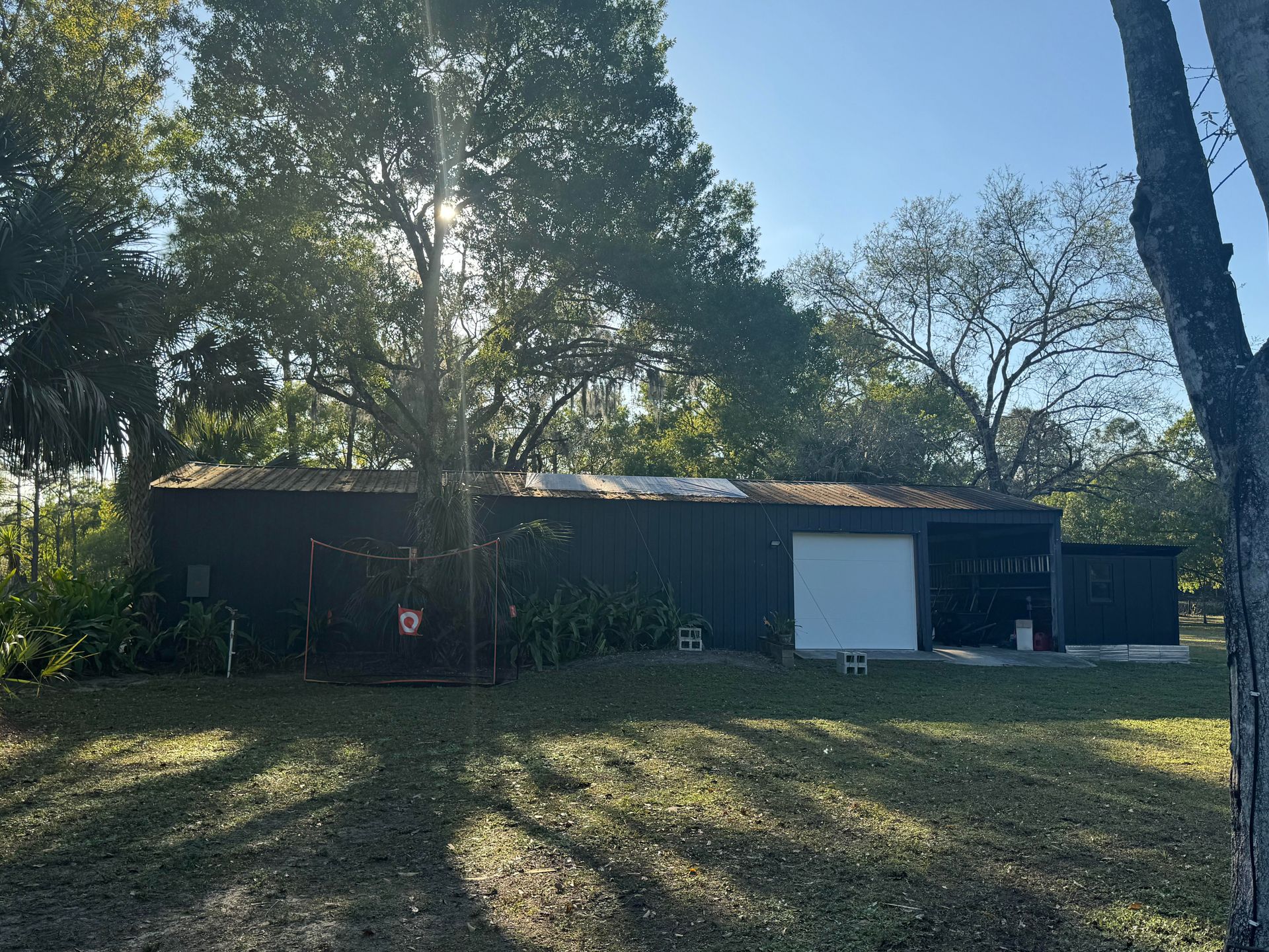 Black shed with a white door, in a sunny grassy area surrounded by trees.