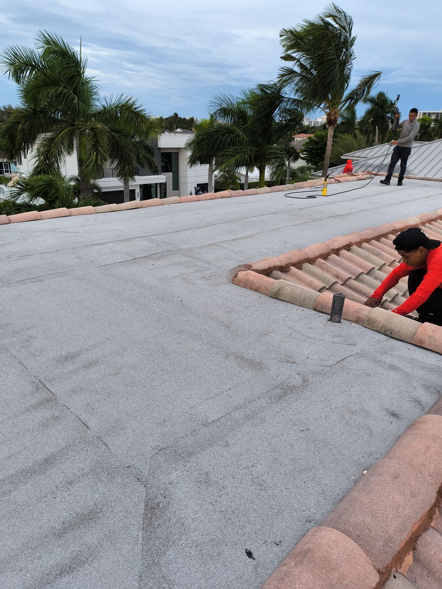 Workers on a roof installing roofing tiles with a cityscape backdrop.