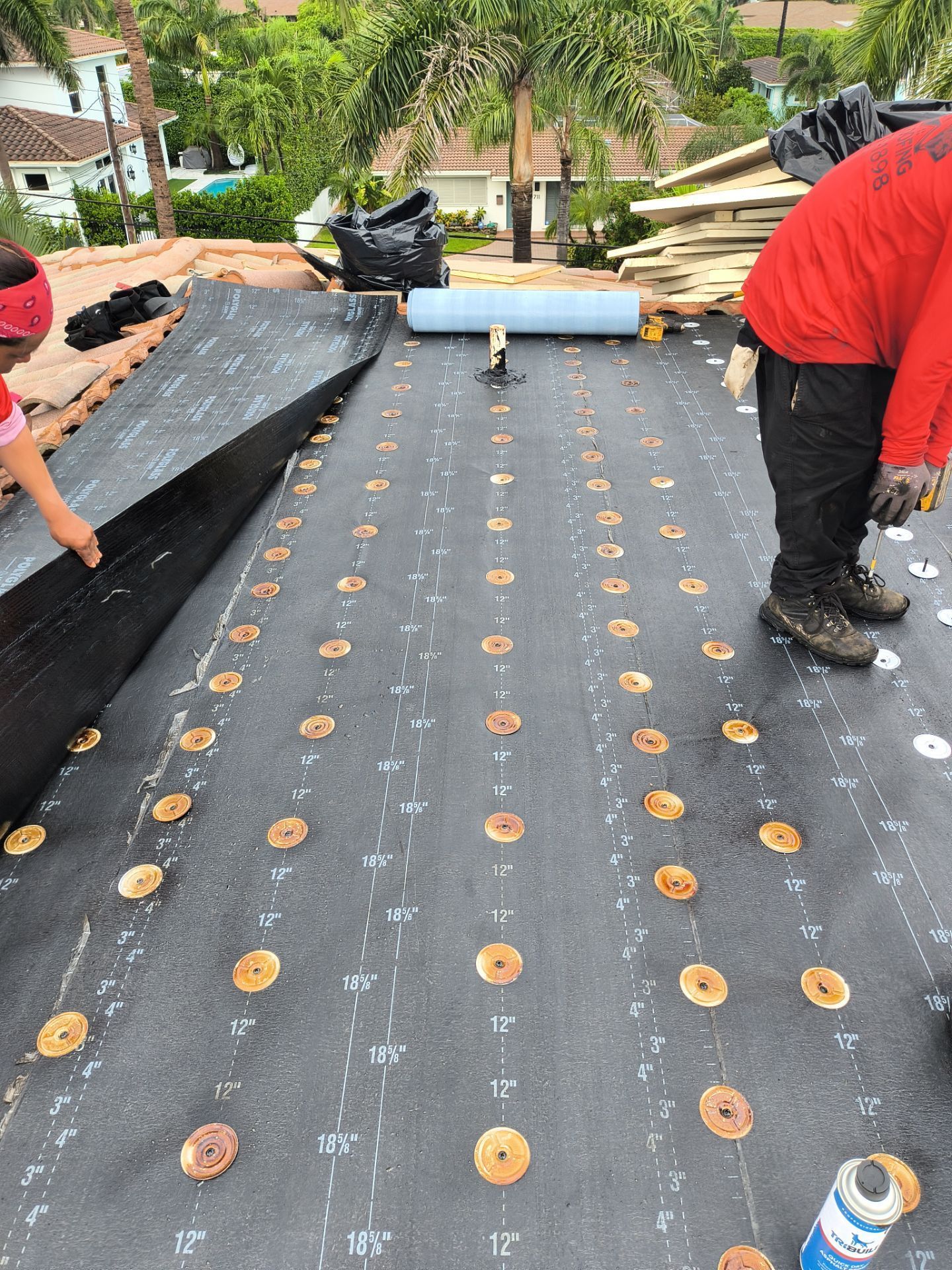 Workers installing roofing material on a rooftop. Black underlayment, gold fasteners.