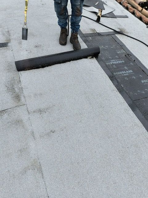 Roofer on a rooftop installing a rolled roofing material.