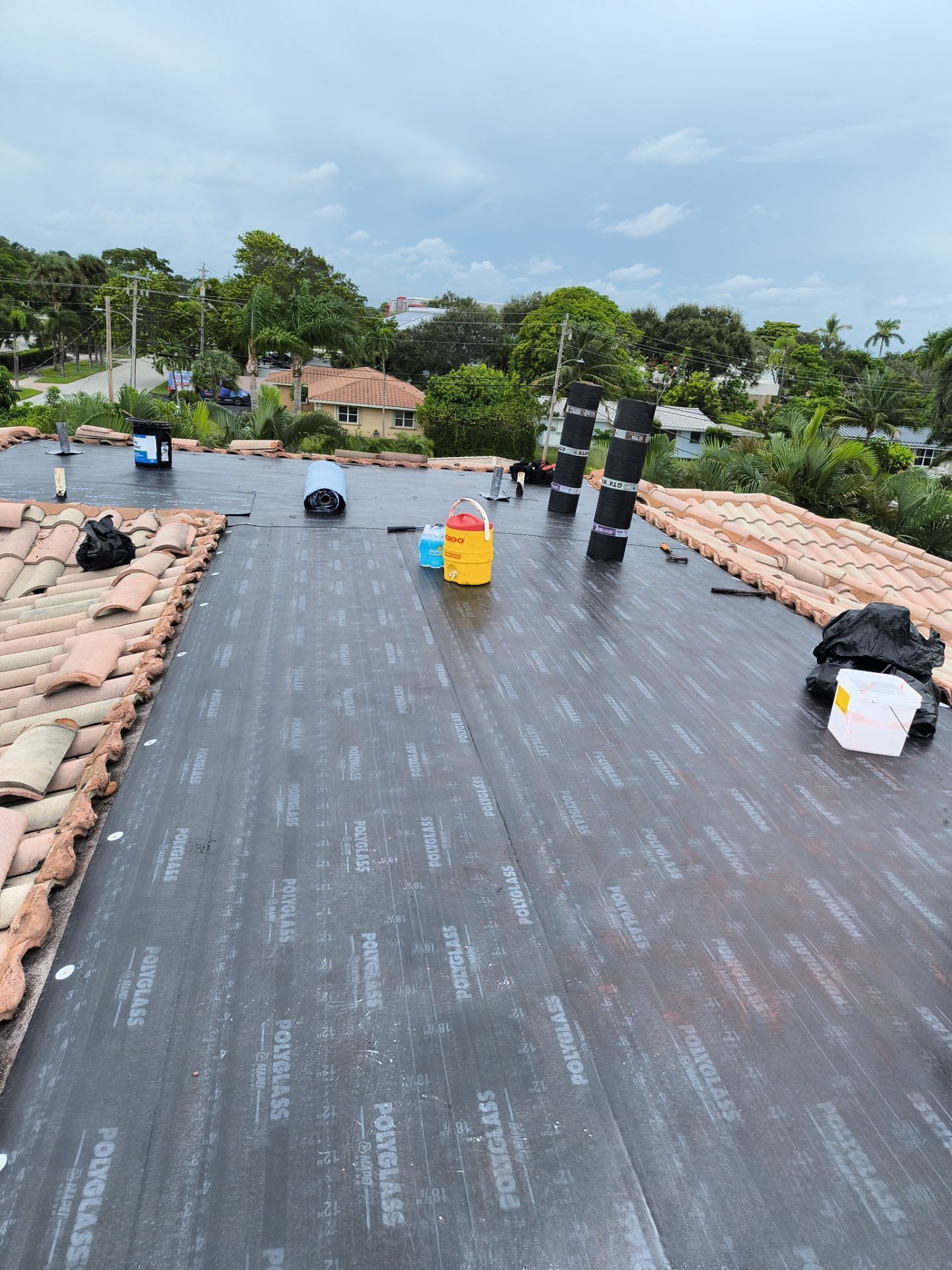 A partially roofed house with dark underlayment, clay tiles, and tools under an overcast sky.