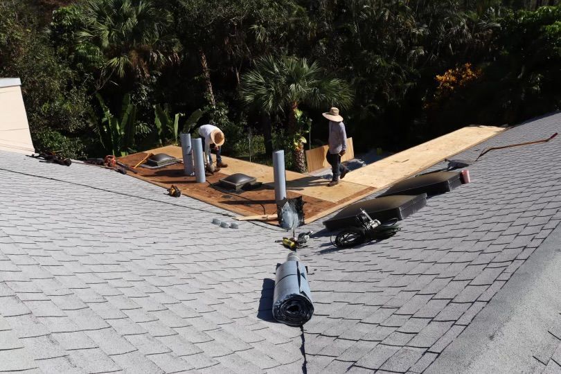 Roofers repairing a roof, working on a wooden section with tools and supplies.