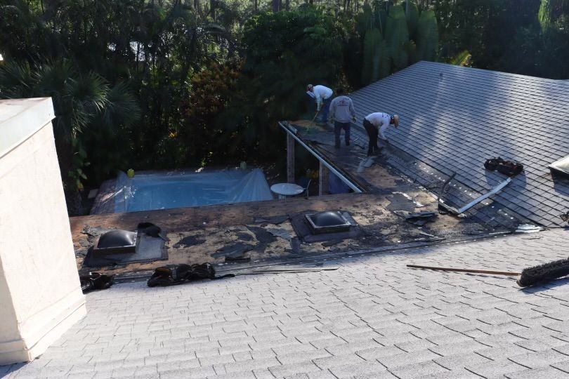 Roofers working on a house roof. Pool and trees in background.