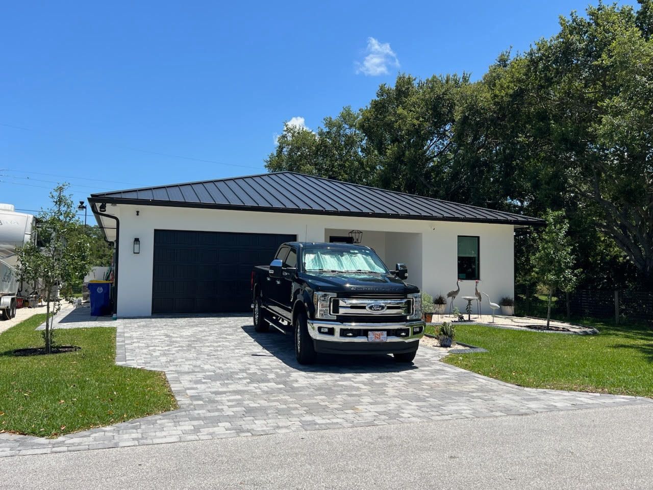 Black truck parked in front of a white house with black garage door and dark roof on a sunny day.
