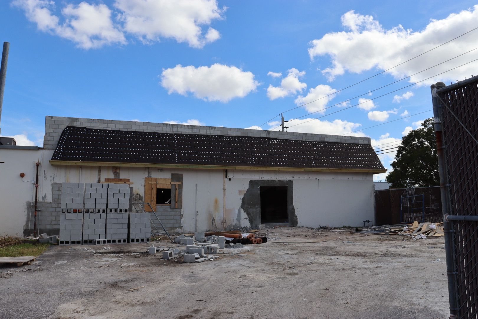 Building under demolition with visible damage, blue sky, and chain link fence.