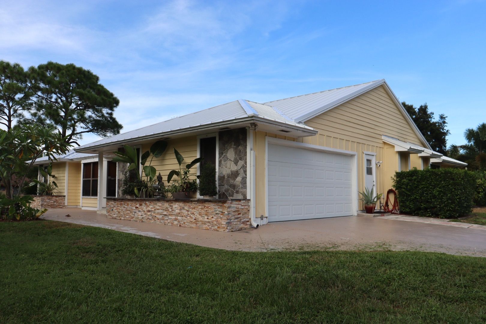 Yellow house with white garage door and roof, on a green lawn under a blue sky.