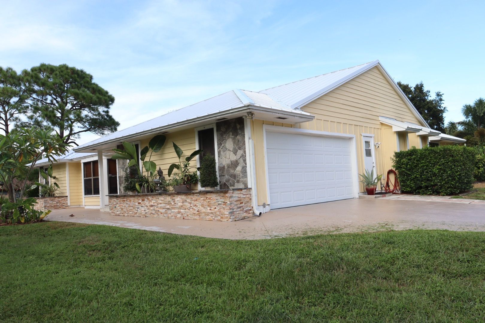 Yellow house with a white garage door and roof; green lawn in the foreground.