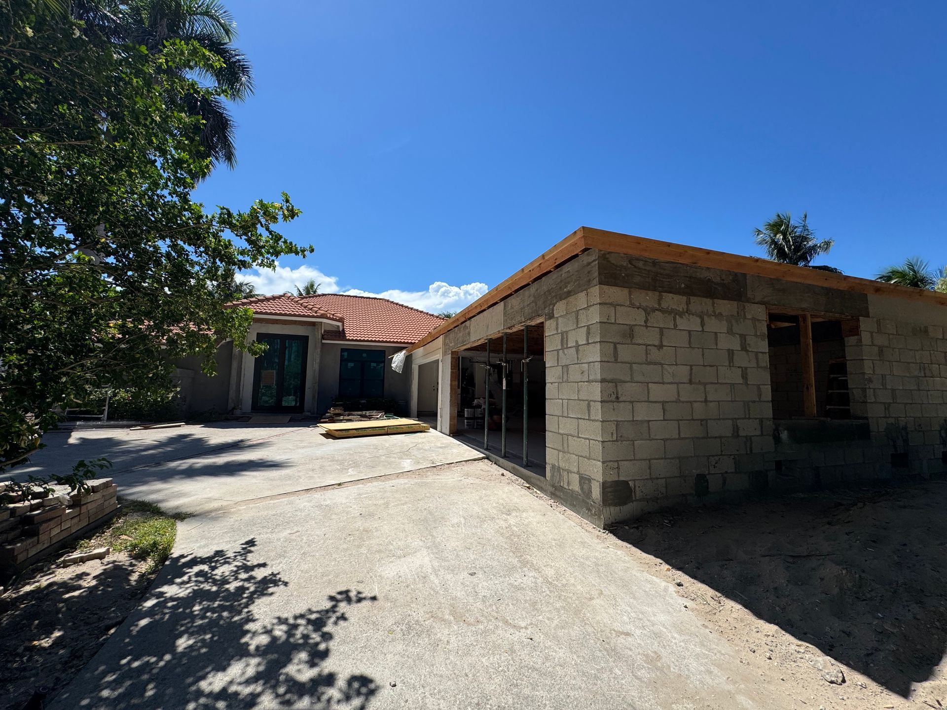 House under construction; concrete block walls, driveway, blue sky.