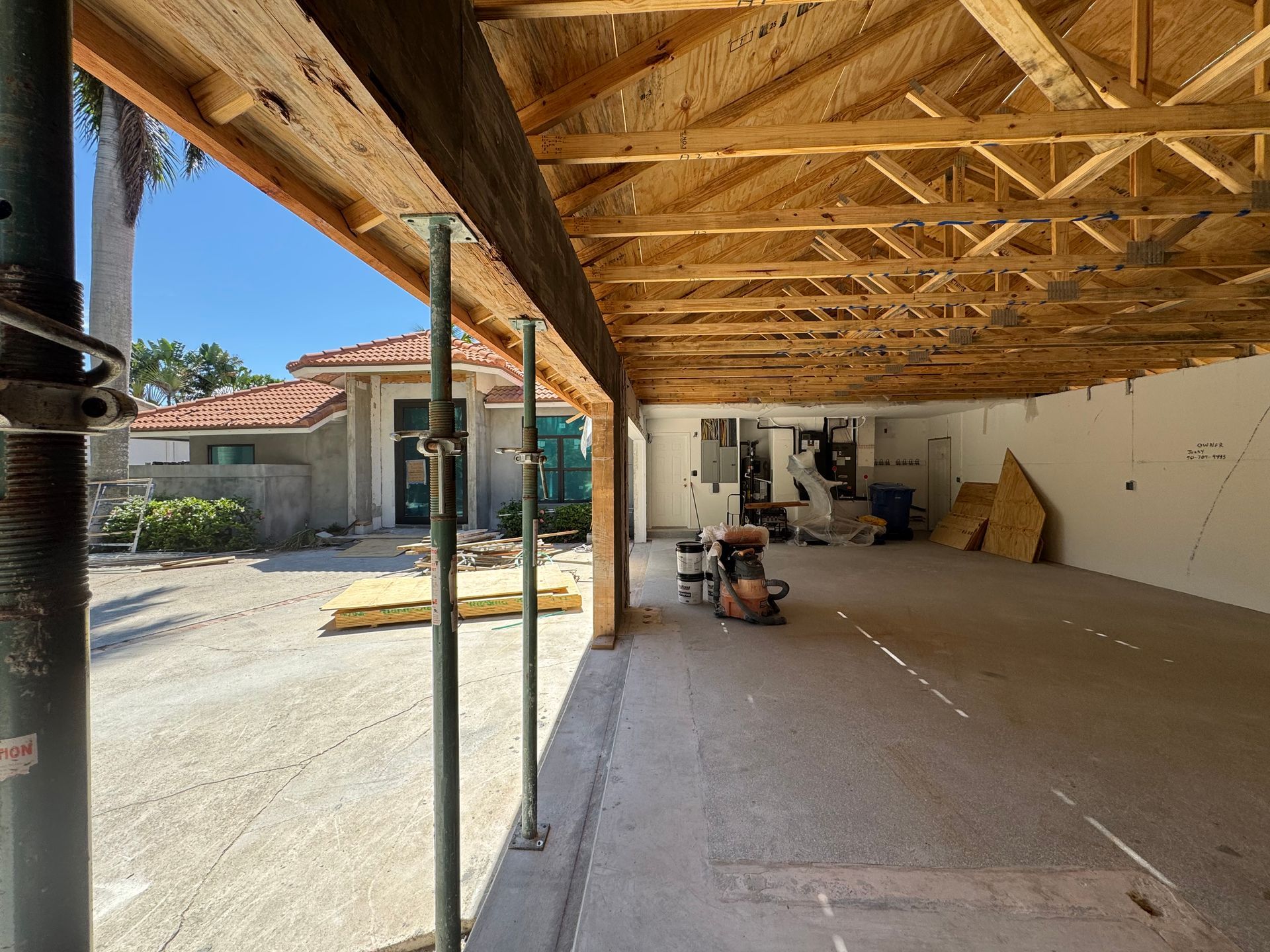 Construction site: garage under renovation, supported by scaffolding, with house in background.