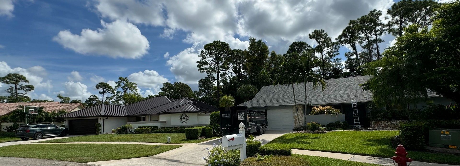 Houses on a suburban street with green lawns and trees under a partly cloudy sky.