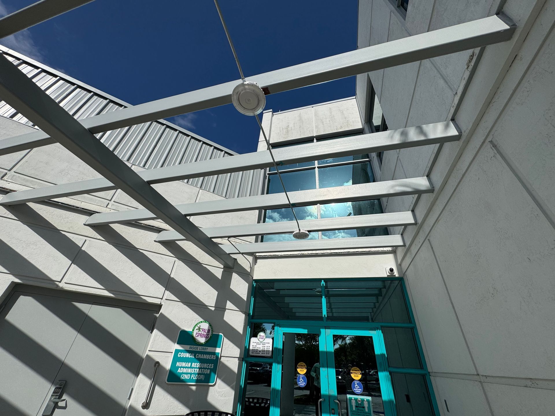 Building entrance with turquoise doors, metal beams, and bright blue sky.