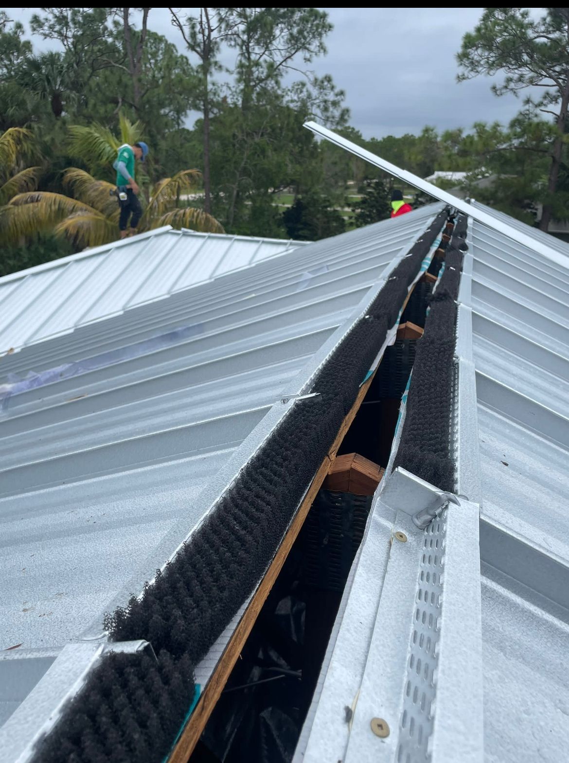 Roof with metal panels and black gutter guards; worker on roof in the background.
