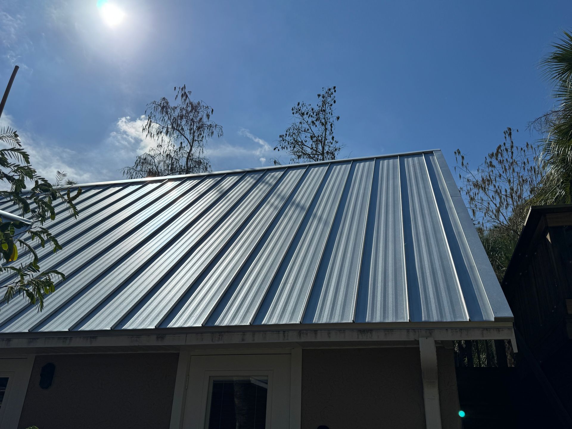 Silver metal roof on a tan building under a bright blue sky.
