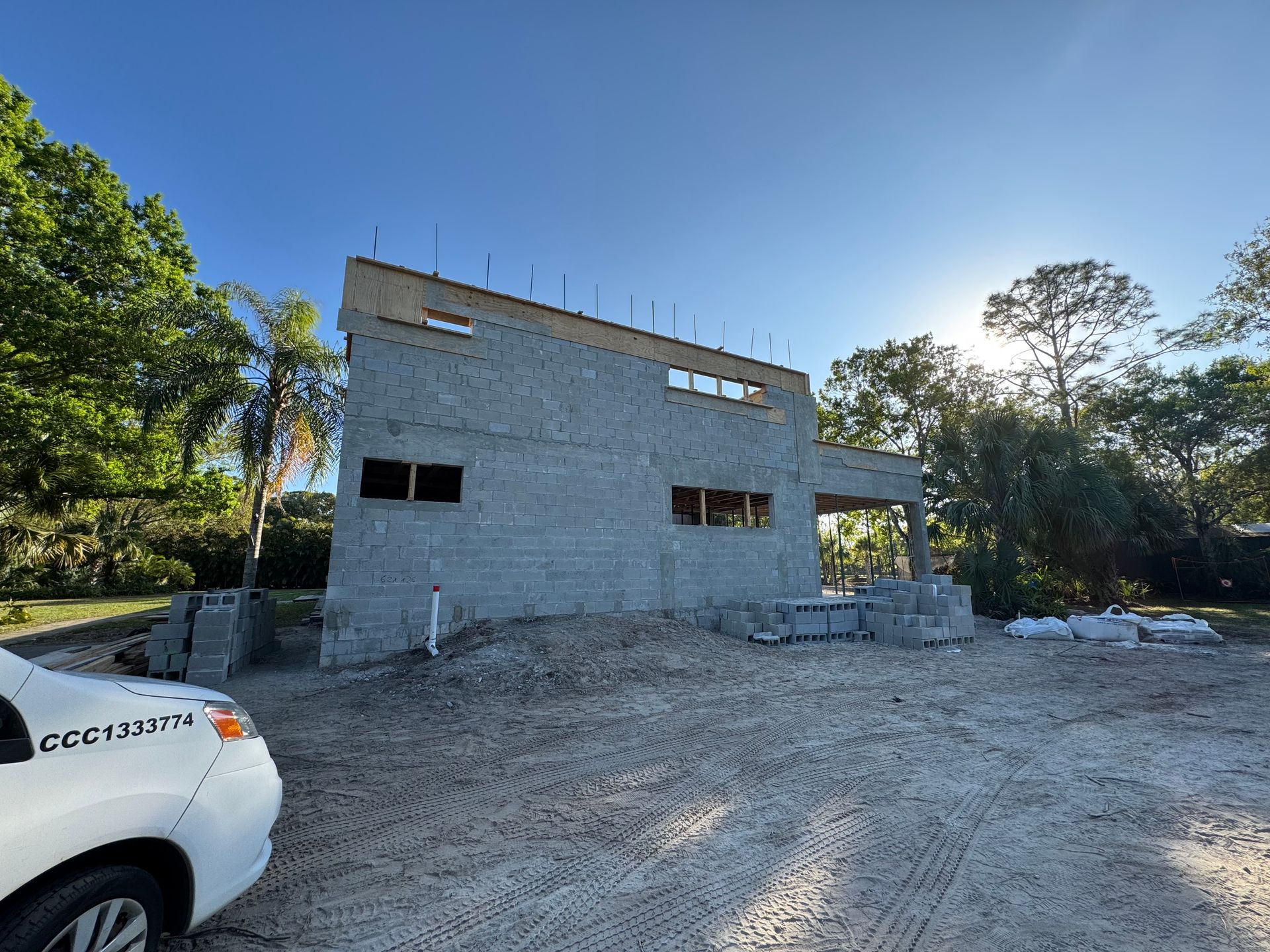Construction site: cinder block building under construction, white van in the foreground, sunny day.