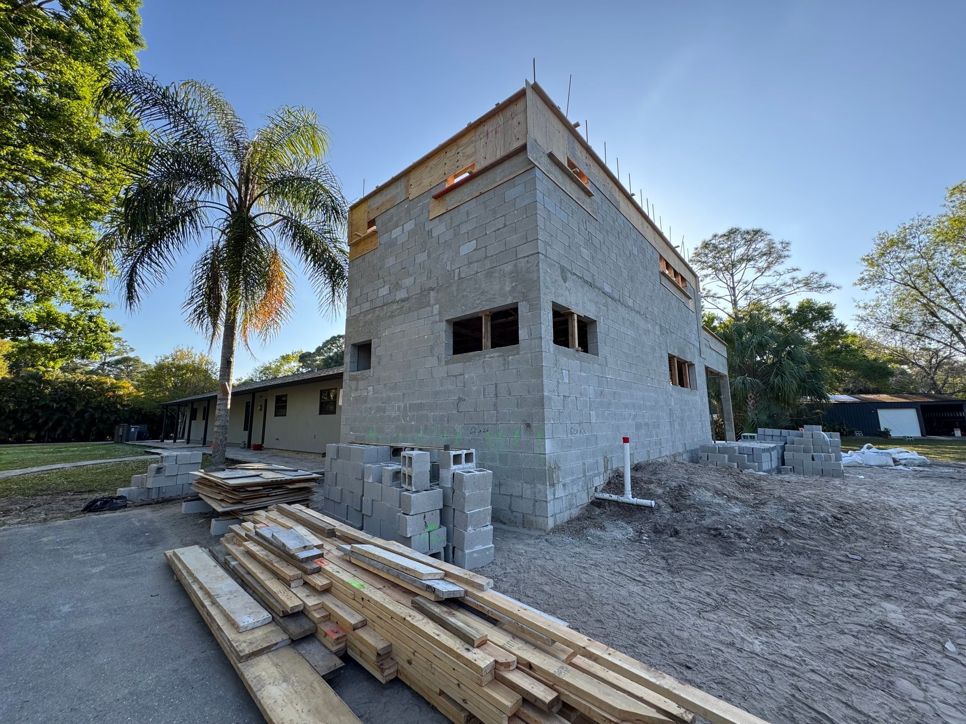 Construction site with unfinished block building, wood beams, and concrete blocks. Sunny outdoor setting.
