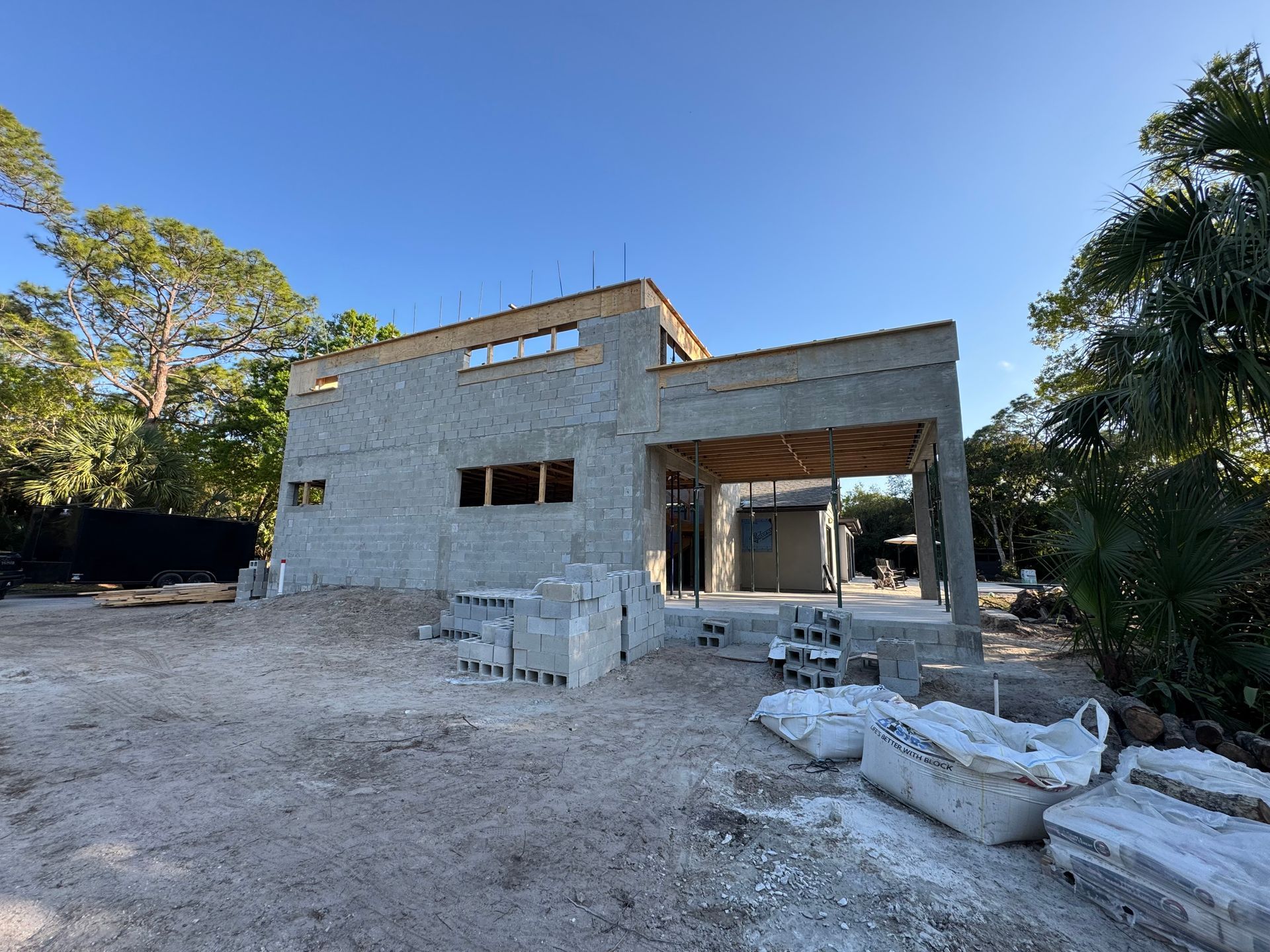 House under construction: concrete block walls, wooden roof framing, and open porch, in a wooded area.