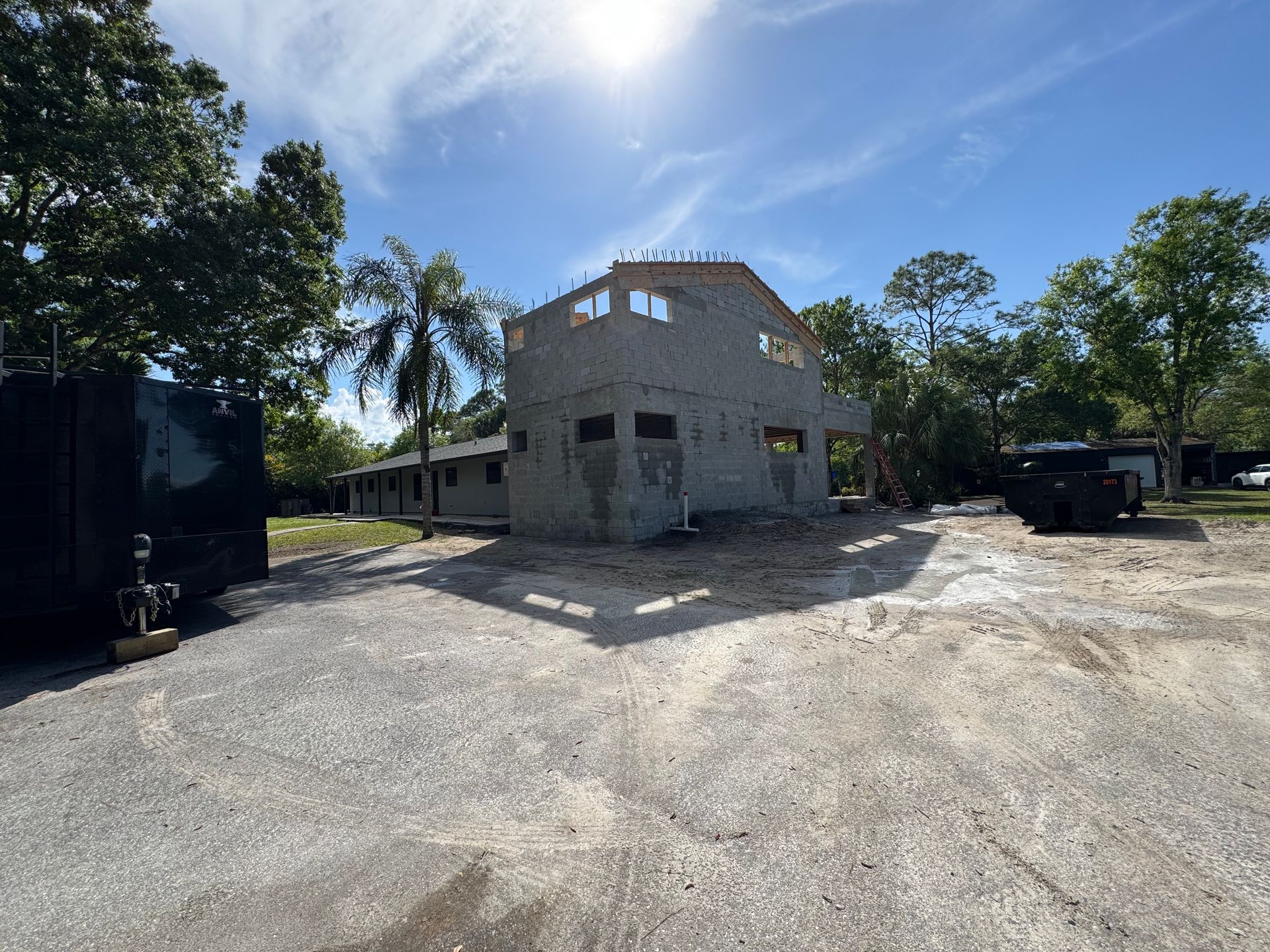 Building under construction, gray concrete walls, unfinished, bright sunlight, blue sky, trees in the background.