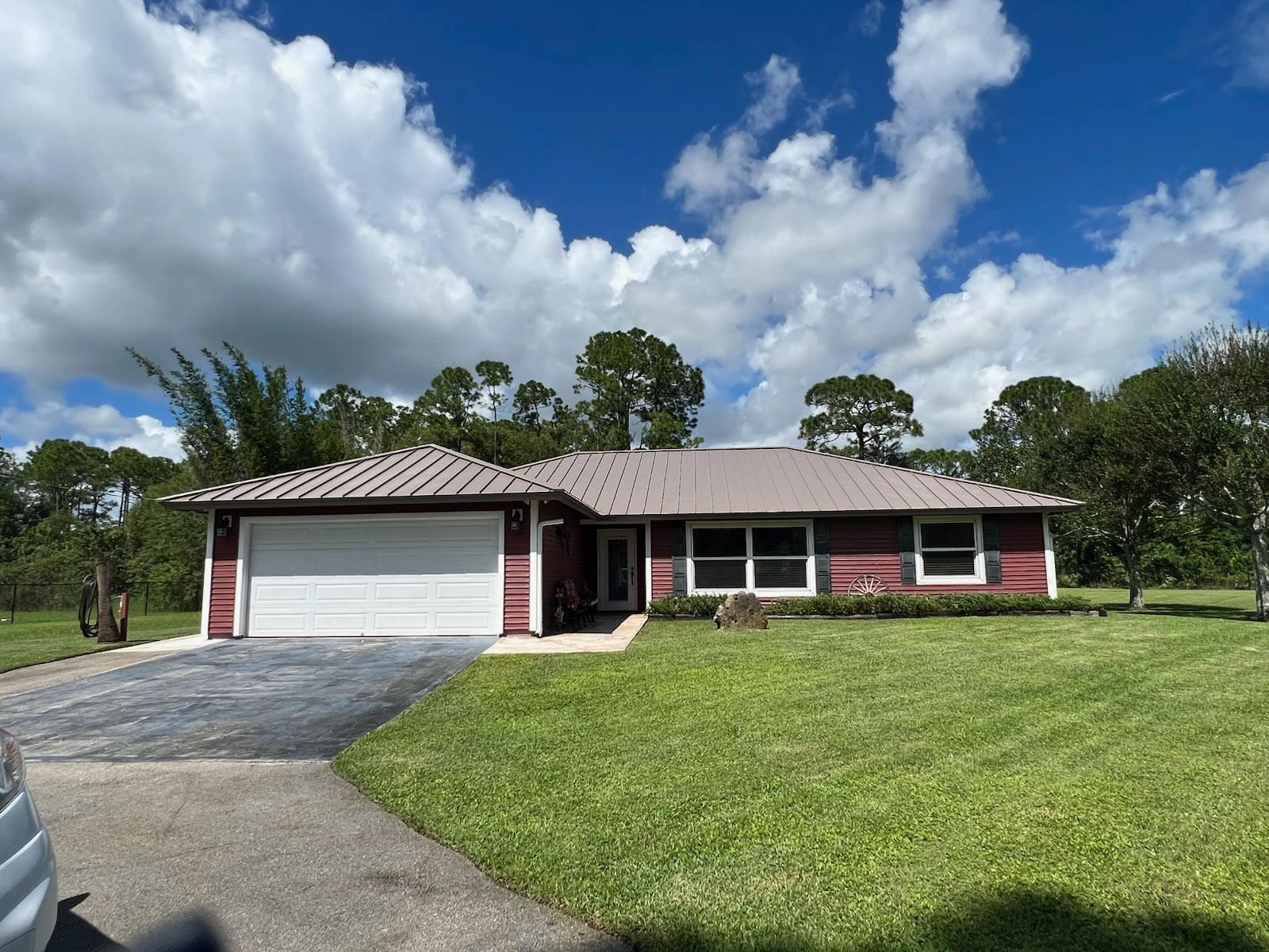 Red house with white garage door, green lawn, and blue sky with clouds.