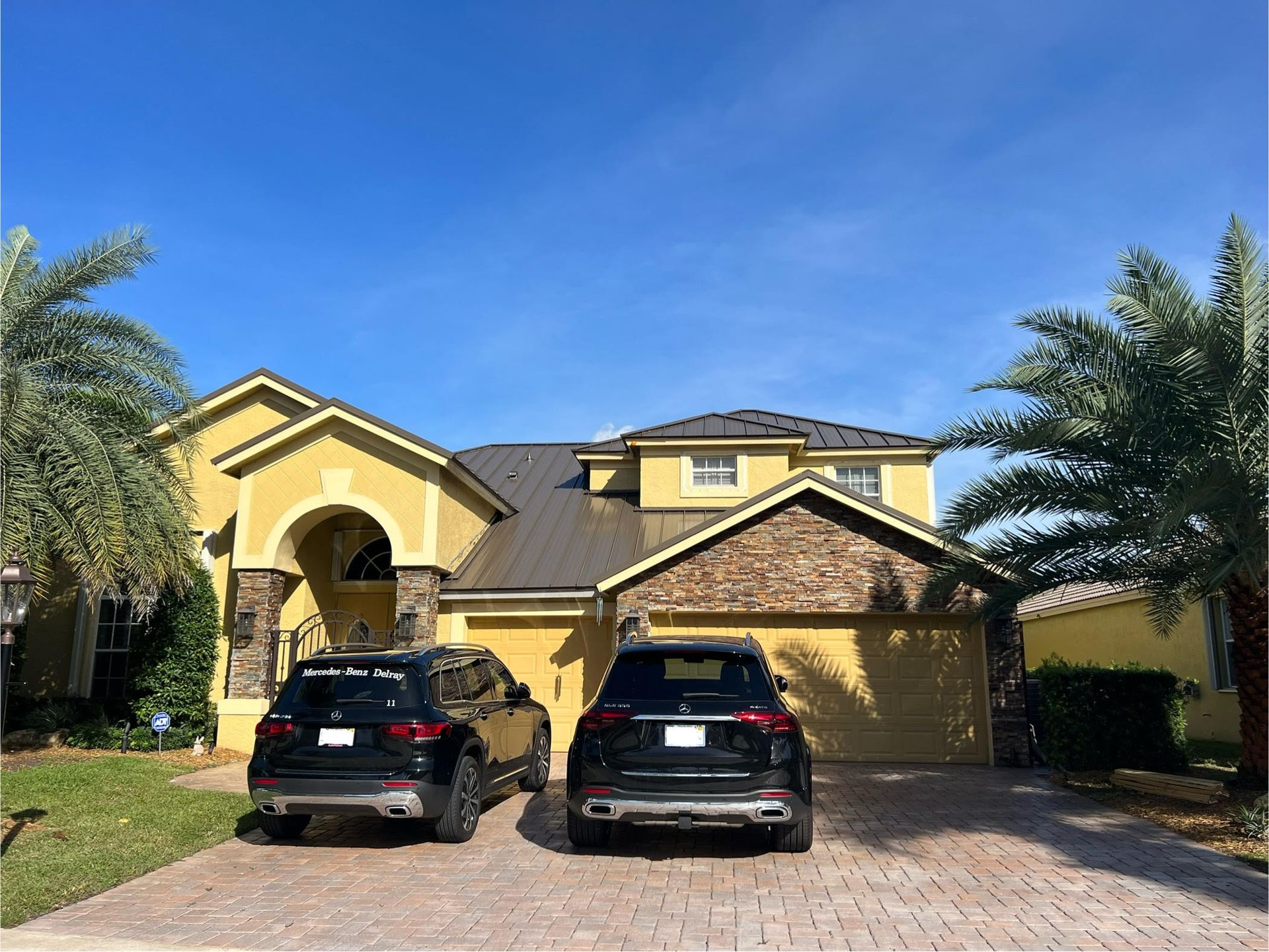 Yellow house with dark cars in driveway under a blue sky.
