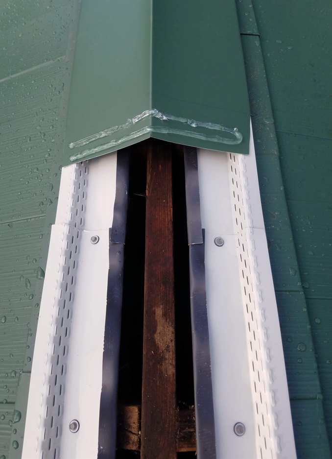 Green roof corner with white vented siding and exposed wood.