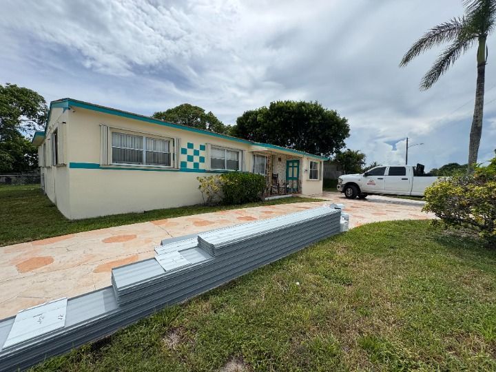 House with stacked metal roofing panels on the lawn, truck in the driveway.