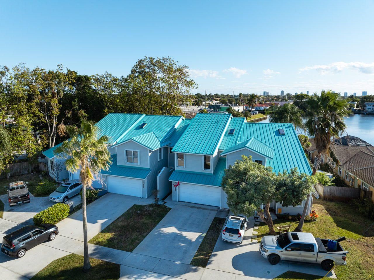 Aerial view of two connected houses with turquoise roofs and driveways; cars parked in front.