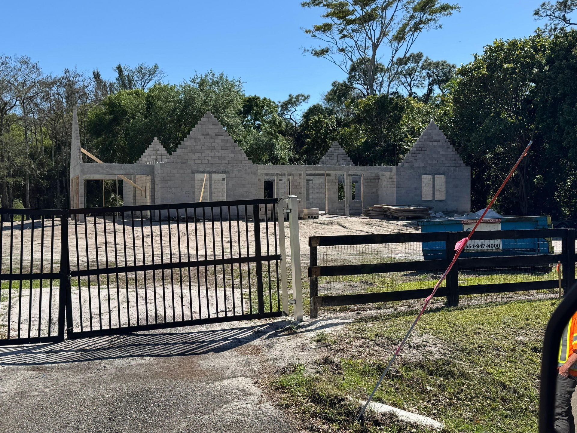 Construction site with concrete block house frame, black gate, and blue dumpster.