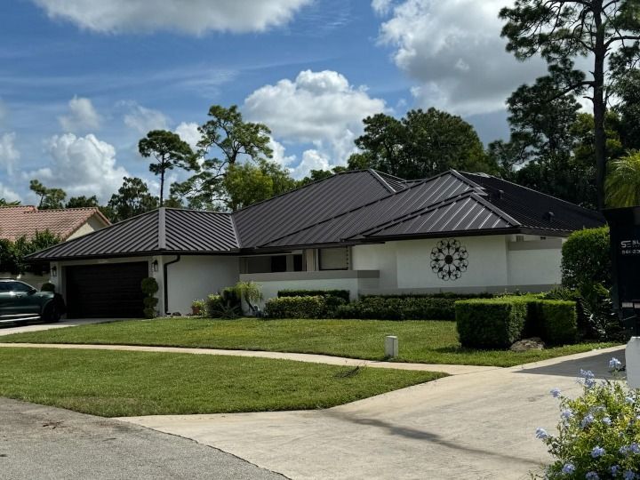 White house with dark roof, green lawn, and driveway on a sunny day.