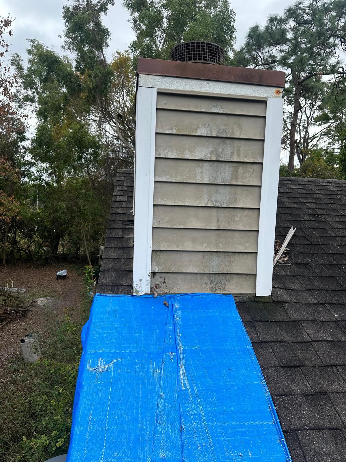 Chimney on a roof with blue tarp. The chimney is gray and white with a nest on top.