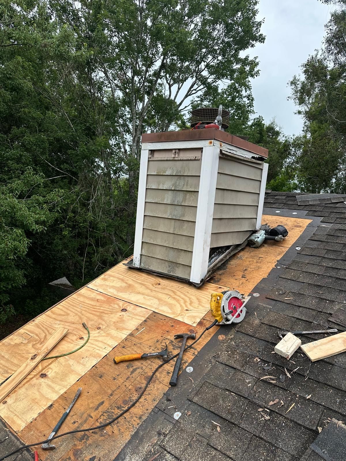 Roof with chimney being repaired; new plywood, tools, and damaged shingles visible.