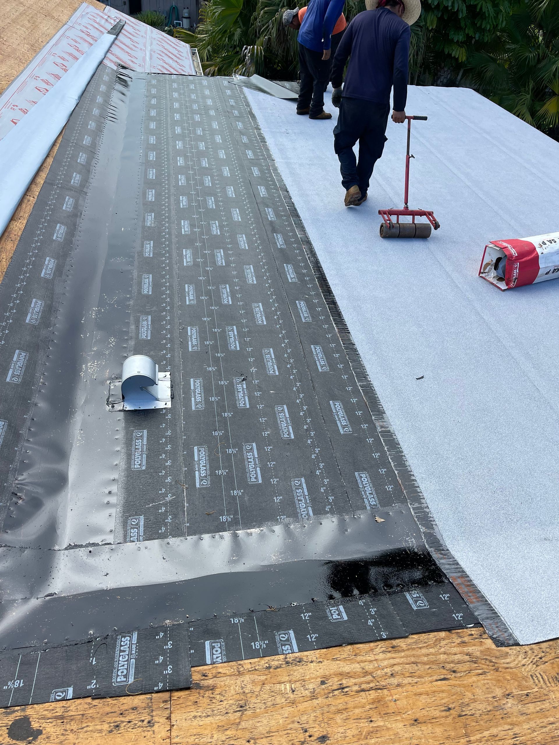 Roofers installing roofing material on a house; dark and light gray roofing layers with people working.