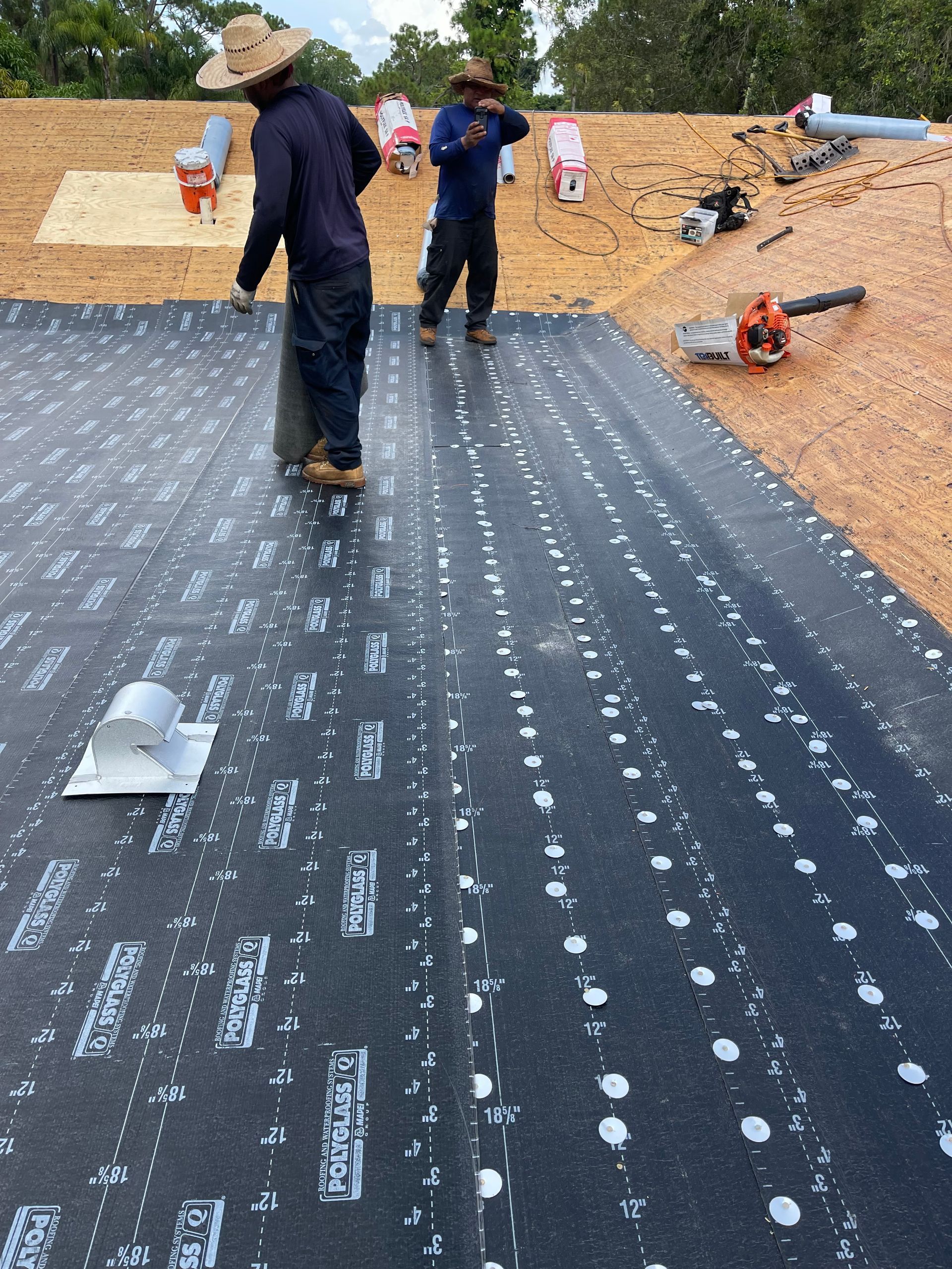 Two workers installing black roofing material on a construction site.