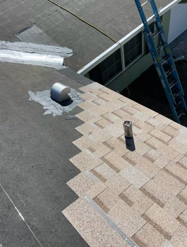 A roof with shingles, a vent pipe, and ladder. Sunlight.