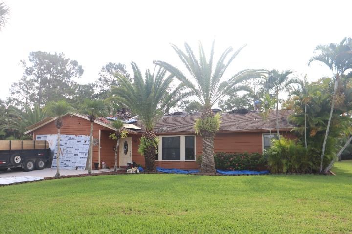 Brick house with palm trees and a trailer on a sunny day; siding is under construction.